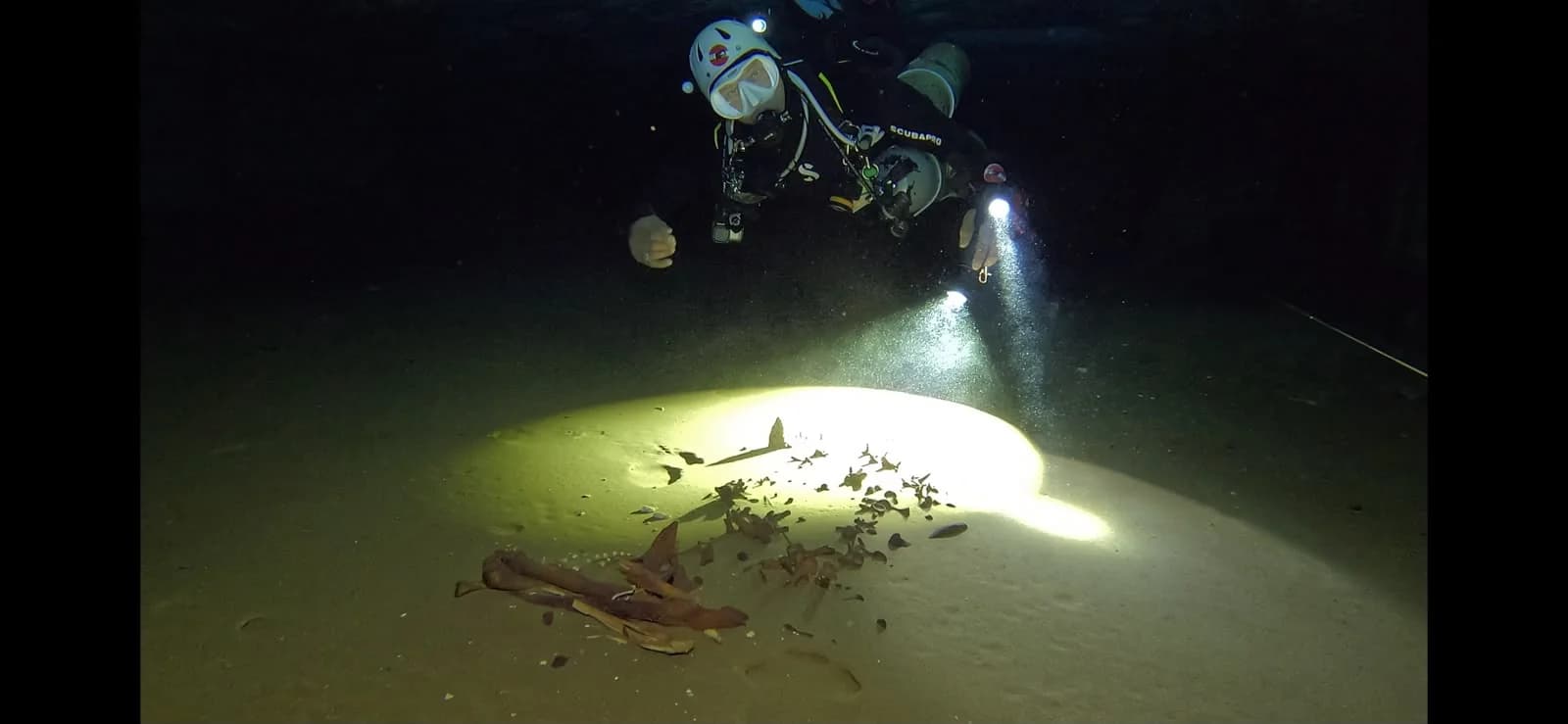 A diver lighting up remains on the cave floor